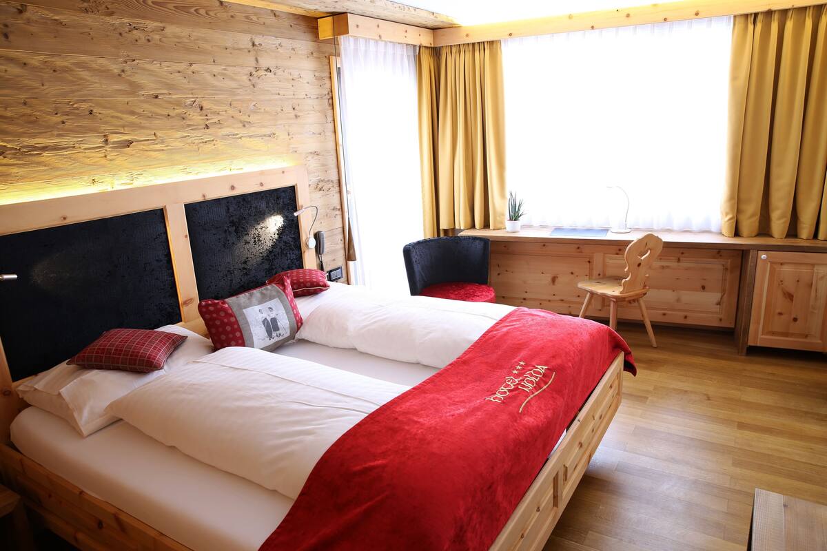 A wooden-framed bed with white and red bedding, a red throw blanket, and a headboard with a black panel.