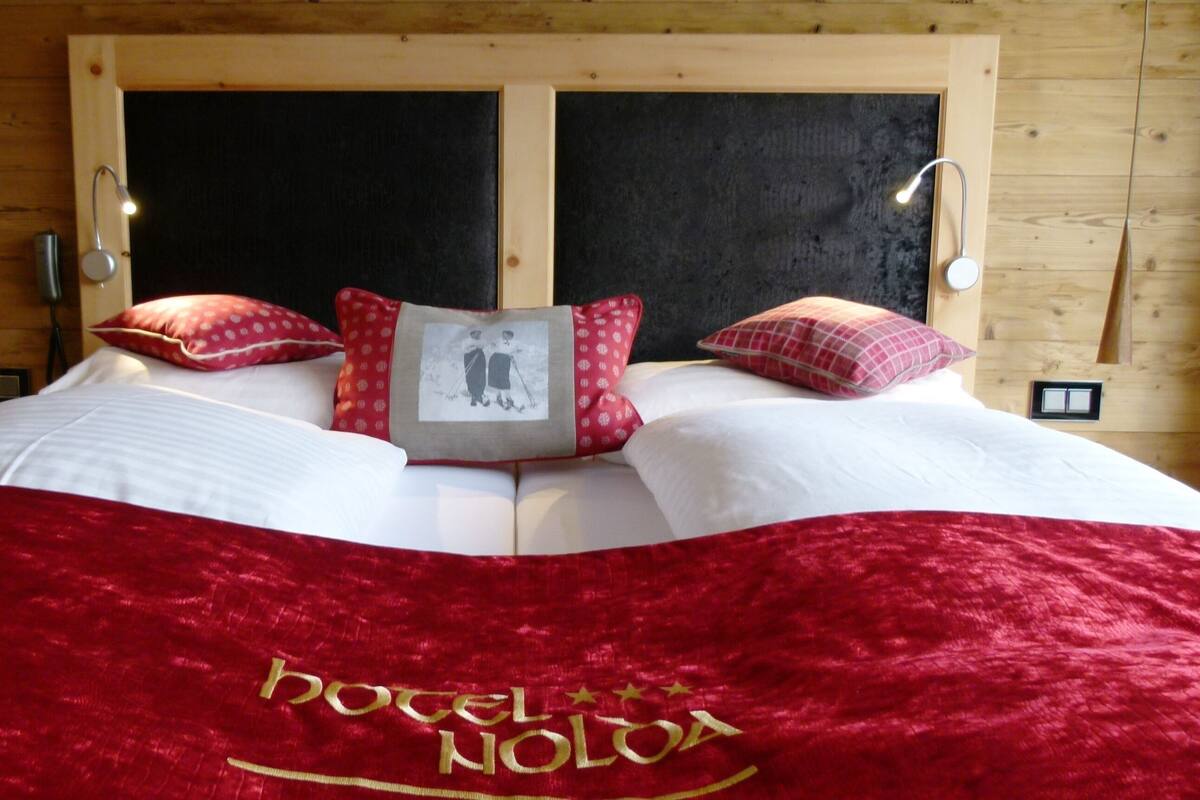 A bed with a red blanket, pillows, and a framed photo.