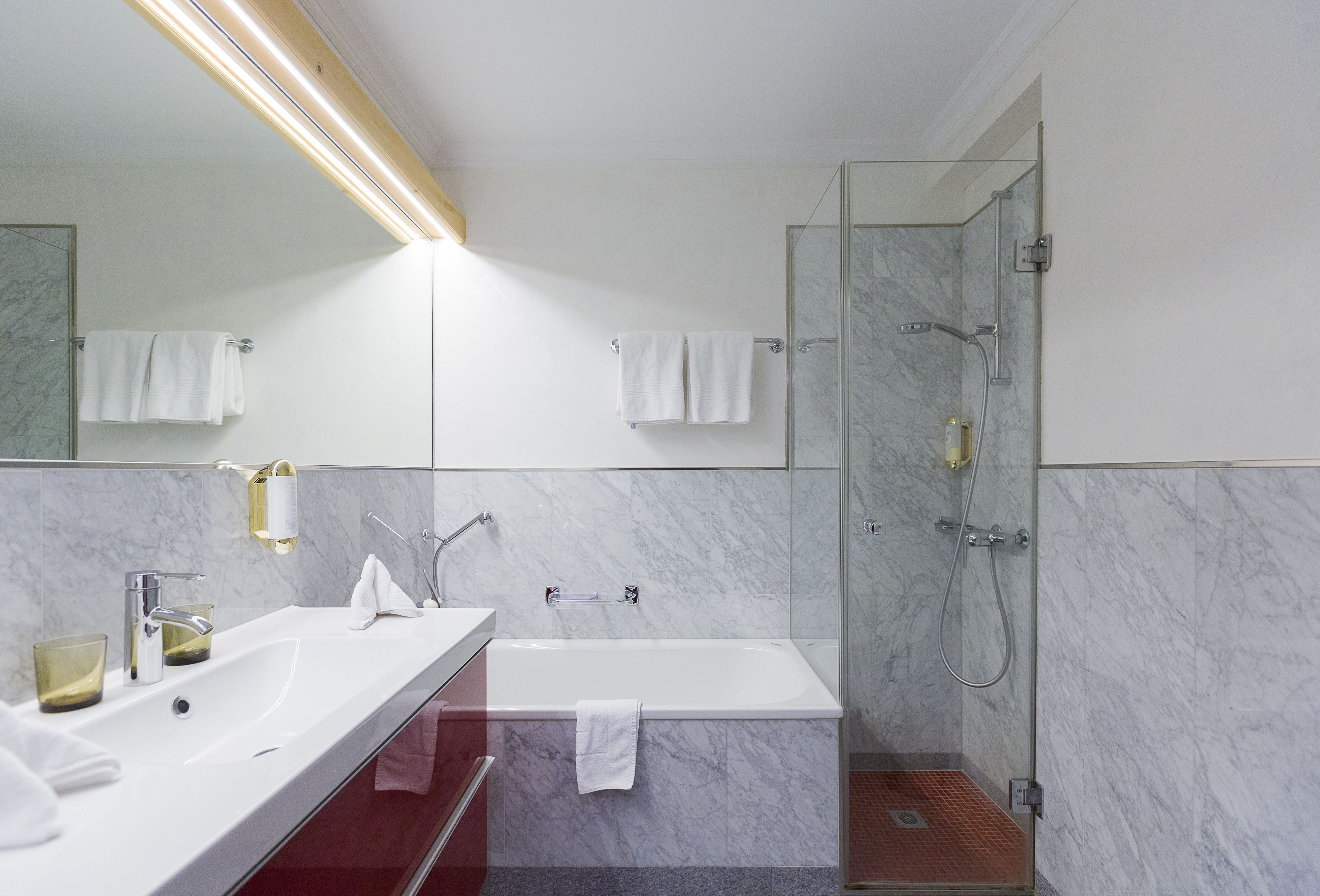 Ein modernes Badezimmer mit einem weißen Waschbecken, einer Glaskabine für die Dusche und einer Wand mit Marmorplatten.