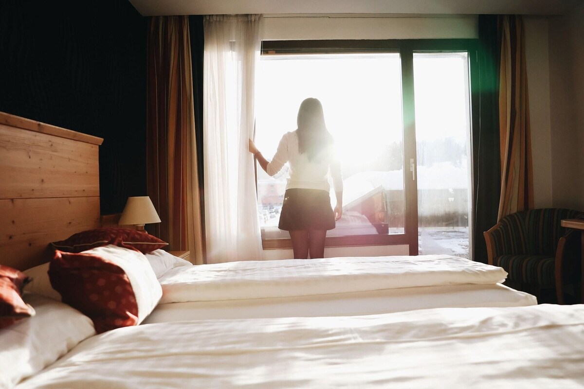 Habitación de hotel con cama, una silla, una lámpara y vistas al exterior.