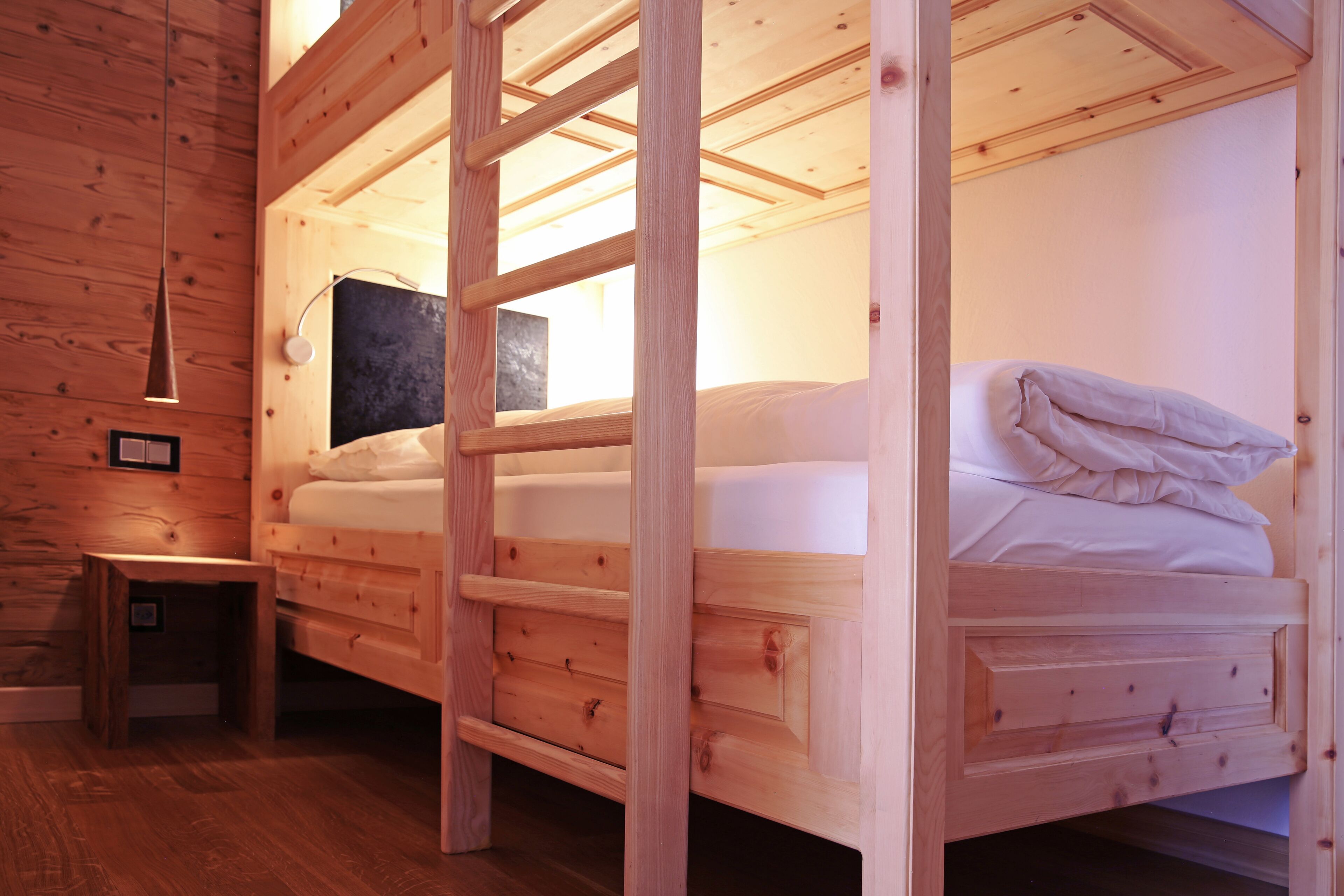 Una cama litera de madera con un mesita de noche y un estante en la pared.