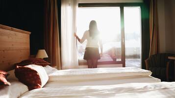 Ein Hotelzimmer mit einem Bett, einem Holz-Kopfteil, einem Stuhl und Blick ins Freie durch eine Glastür.
