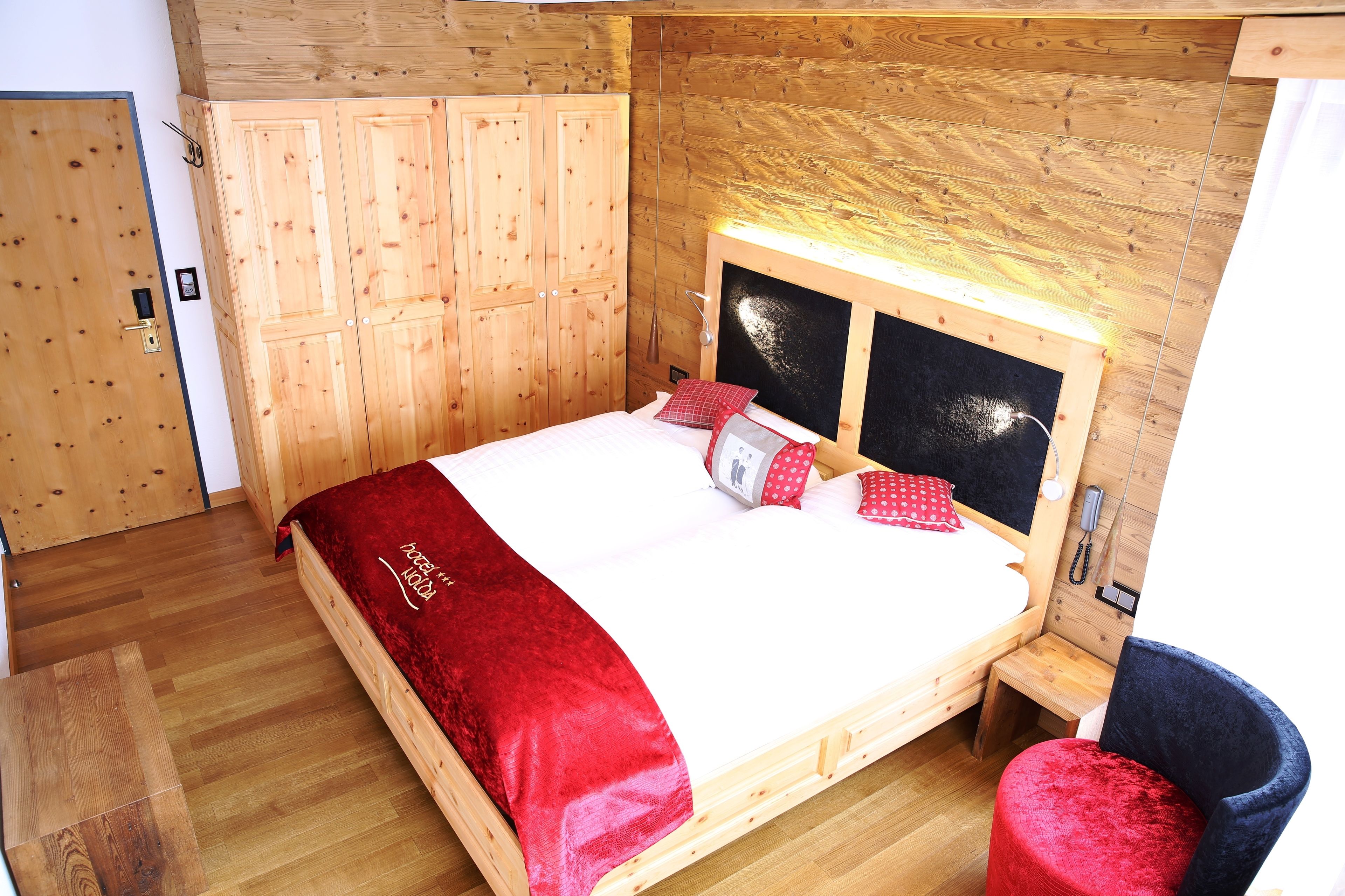 A wooden bunk bed with a red blanket, a wooden wardrobe, and a small wooden table.