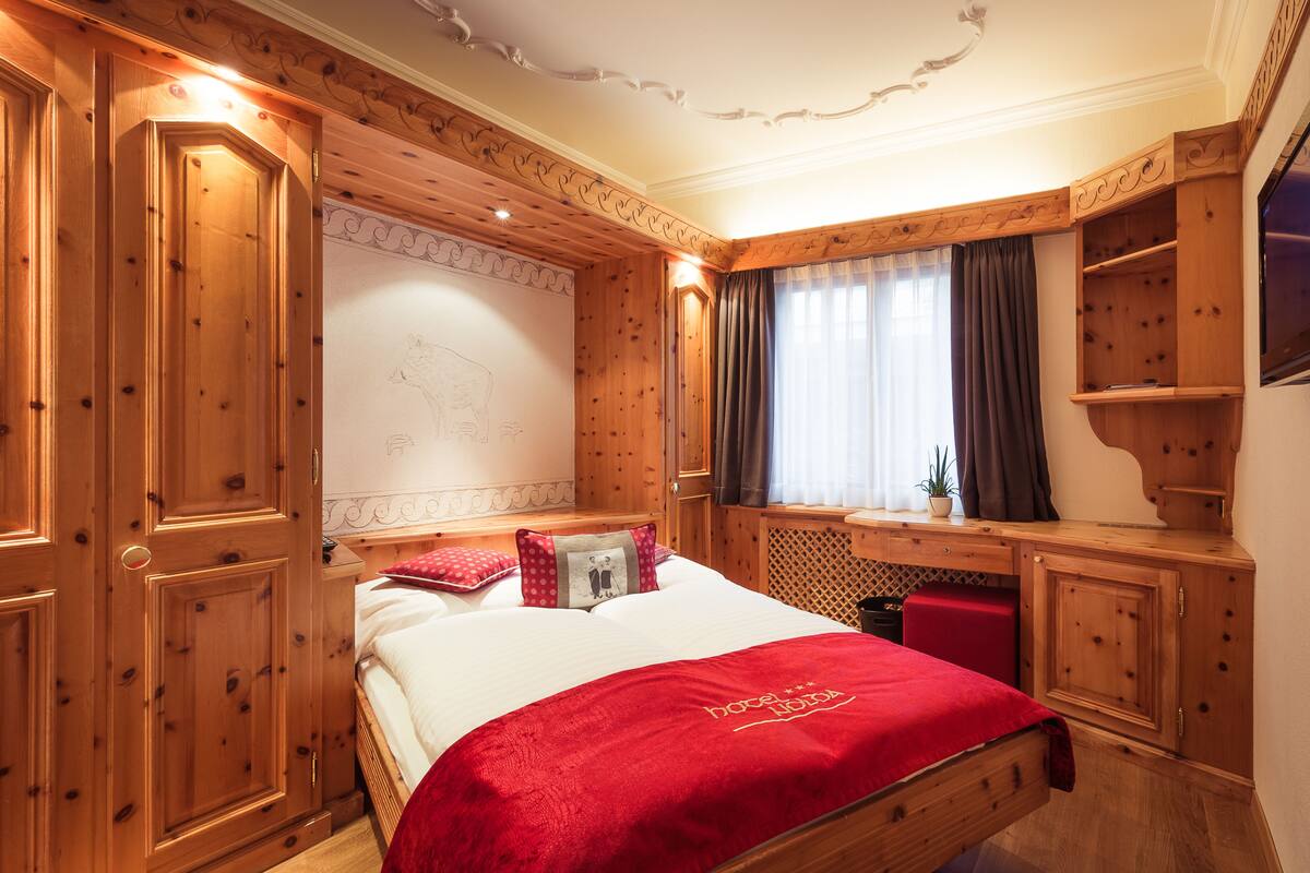 A wooden-paneled room with a bed, a desk, and a television.