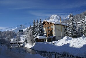 A hotel with a wooden facade, a ski lift in the background, and a snow-covered landscape.