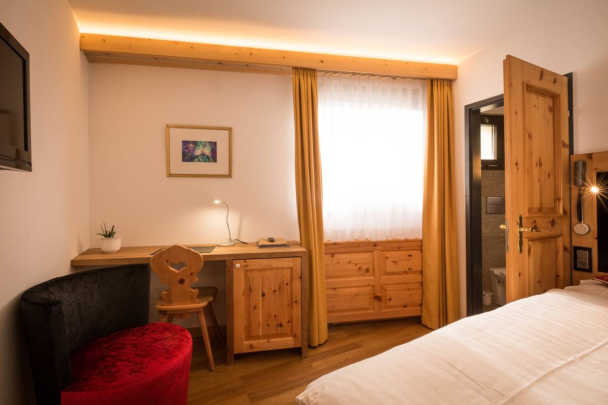 A bedroom with a wooden desk, a chair, a bed, and a wardrobe.