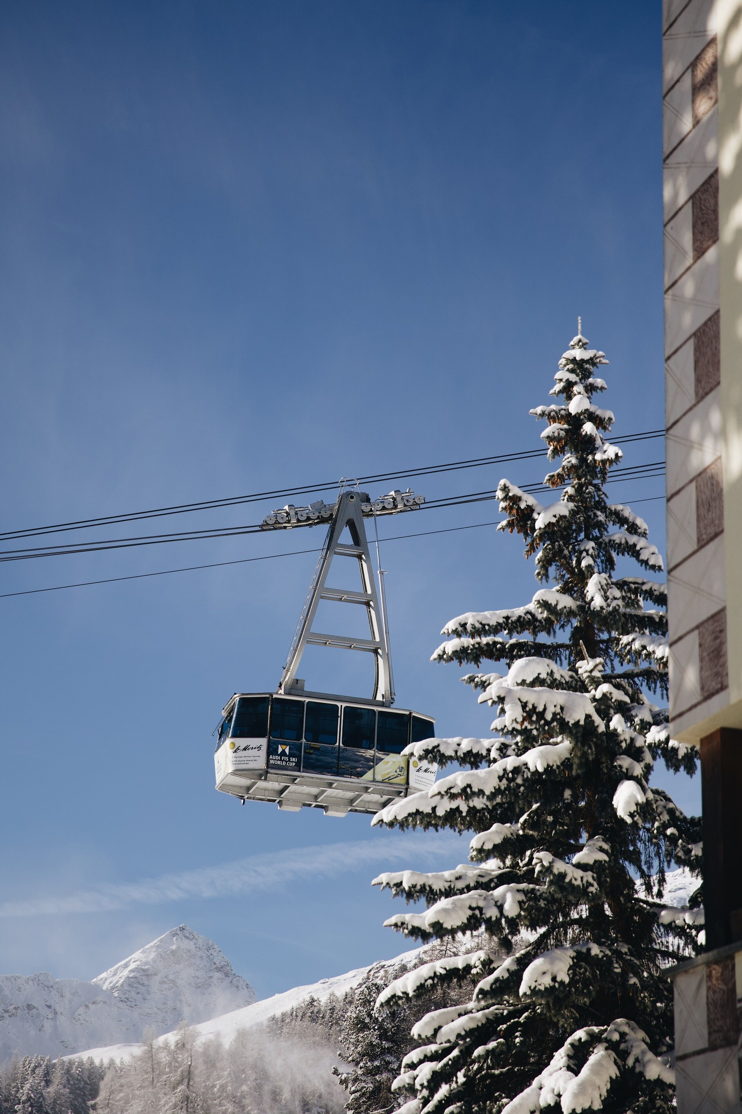 A cable car suspended over a snowy landscape with mountains in the background.