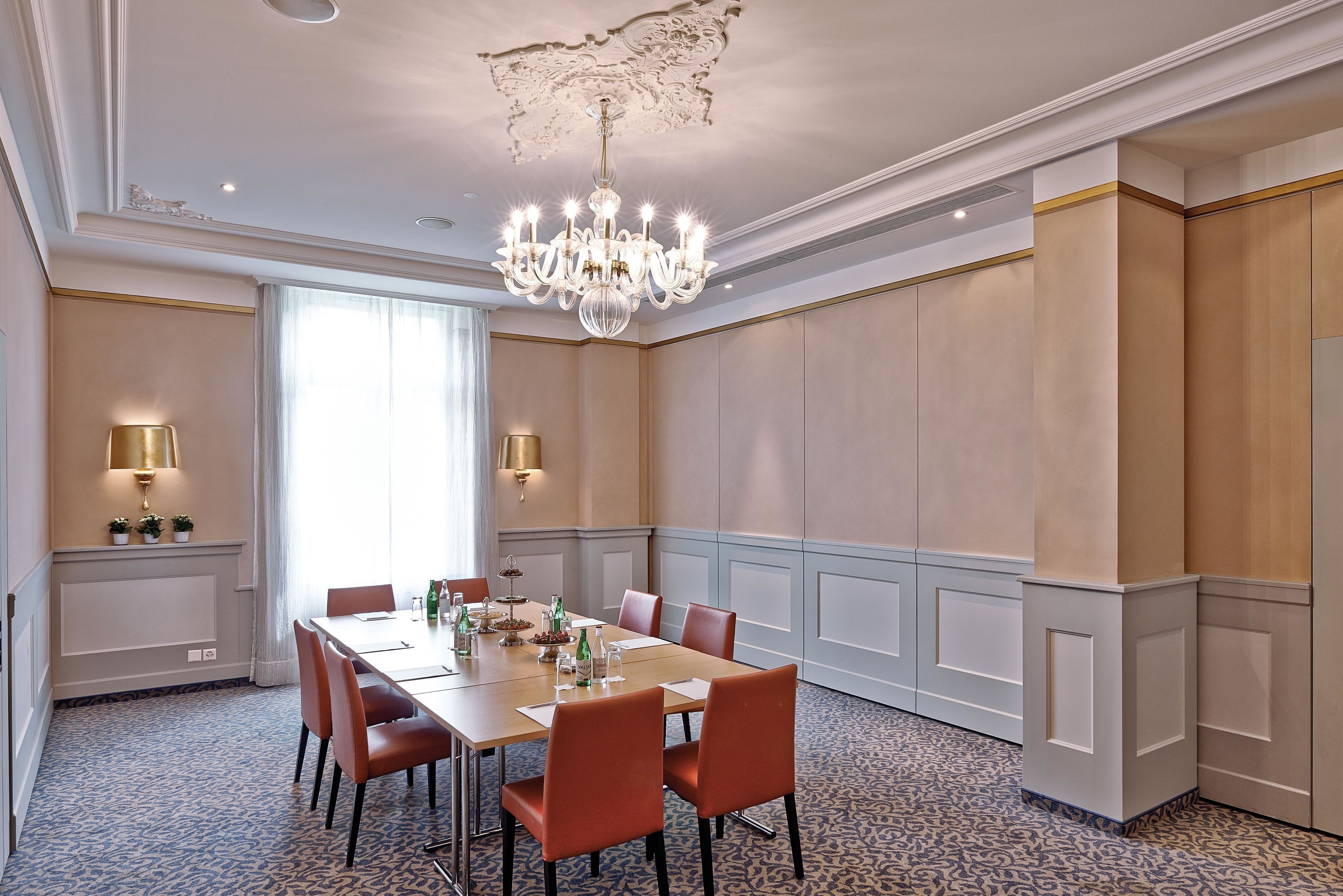 A conference room with a long table, chairs, a chandelier, and wall-mounted lamps.
