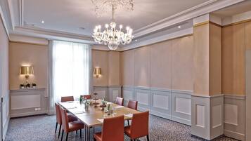 A conference room with a long table, chairs, a chandelier, and wall-mounted lamps.
