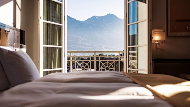 A bedroom with a bed, a view of mountains, and a balcony with a railing.