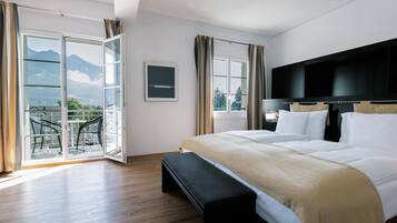 Quarto com cama, um banquinho, televisão e varanda com vista para as montanhas.