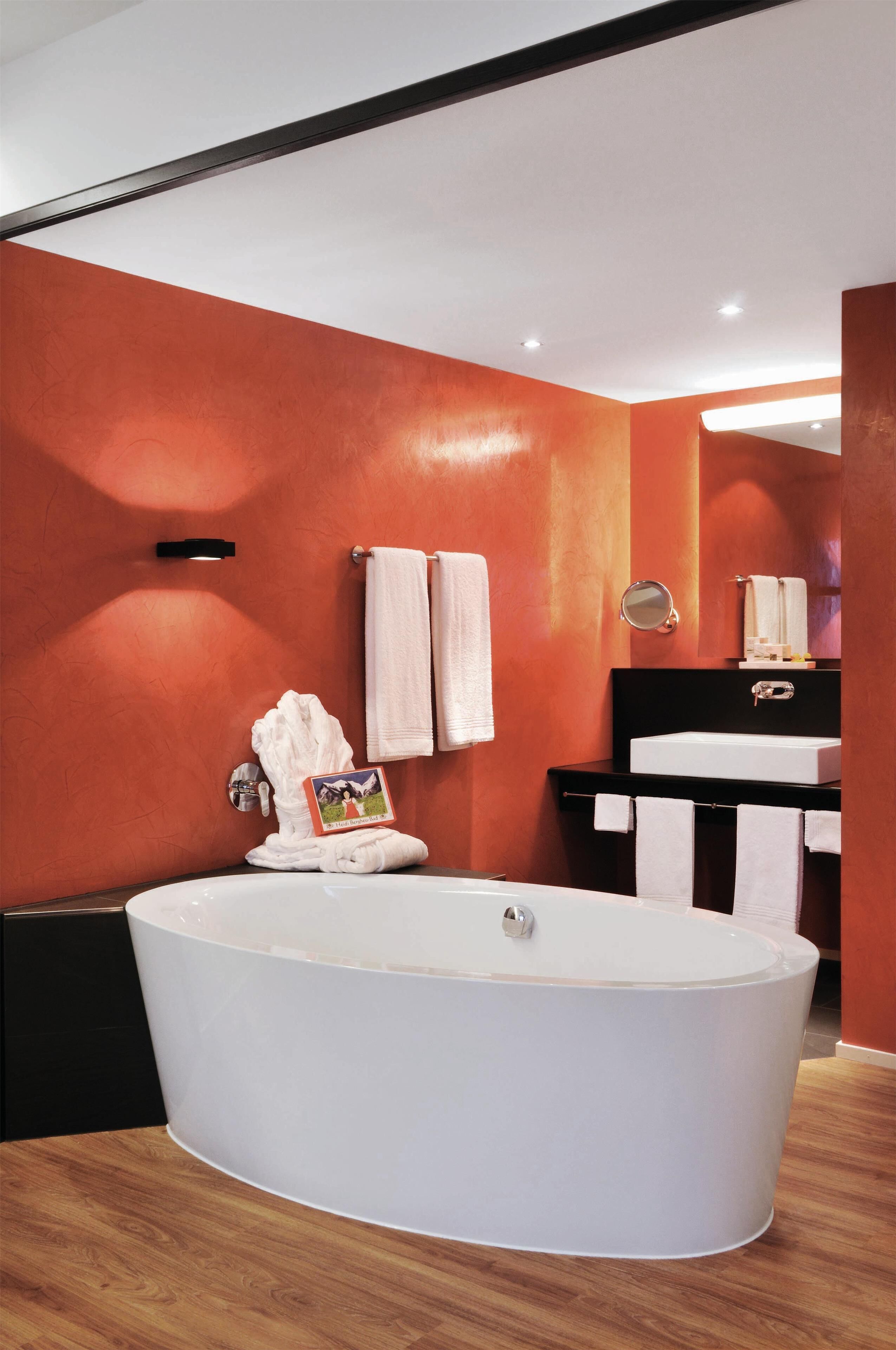 Ein modernes Badezimmer mit einer freistehenden Badewanne, einem schwarzen Waschtisch mit Spiegel und orangefarbenen Wänden.