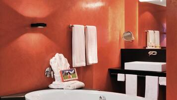 Ein modernes Badezimmer mit einer freistehenden Badewanne, einem schwarzen Waschtisch mit Spiegel und orangefarbenen Wänden.