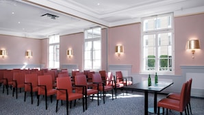 A conference room with rows of red chairs, a table, and large windows with natural light.
