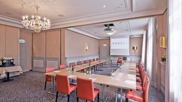 A conference room with a long table, red chairs, a chandelier, and a projector screen.