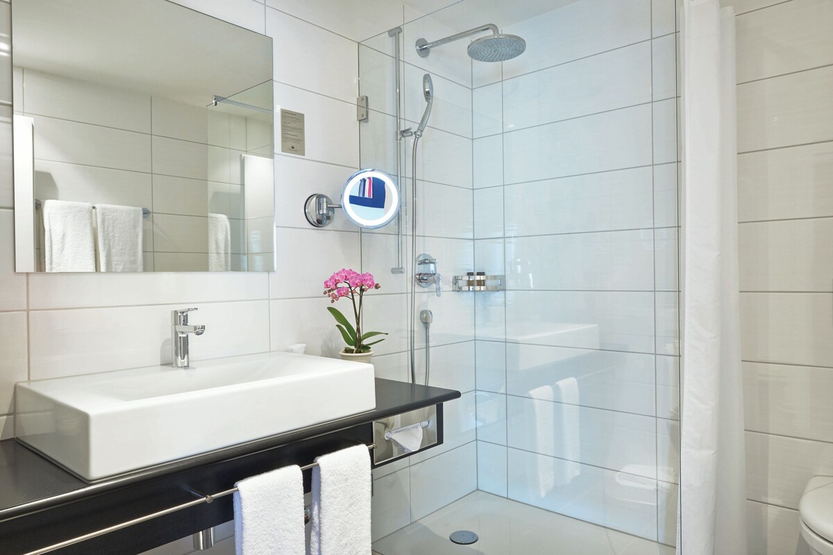 A modern bathroom with a white sink, a large mirror, a glass shower enclosure, and a potted orchid.