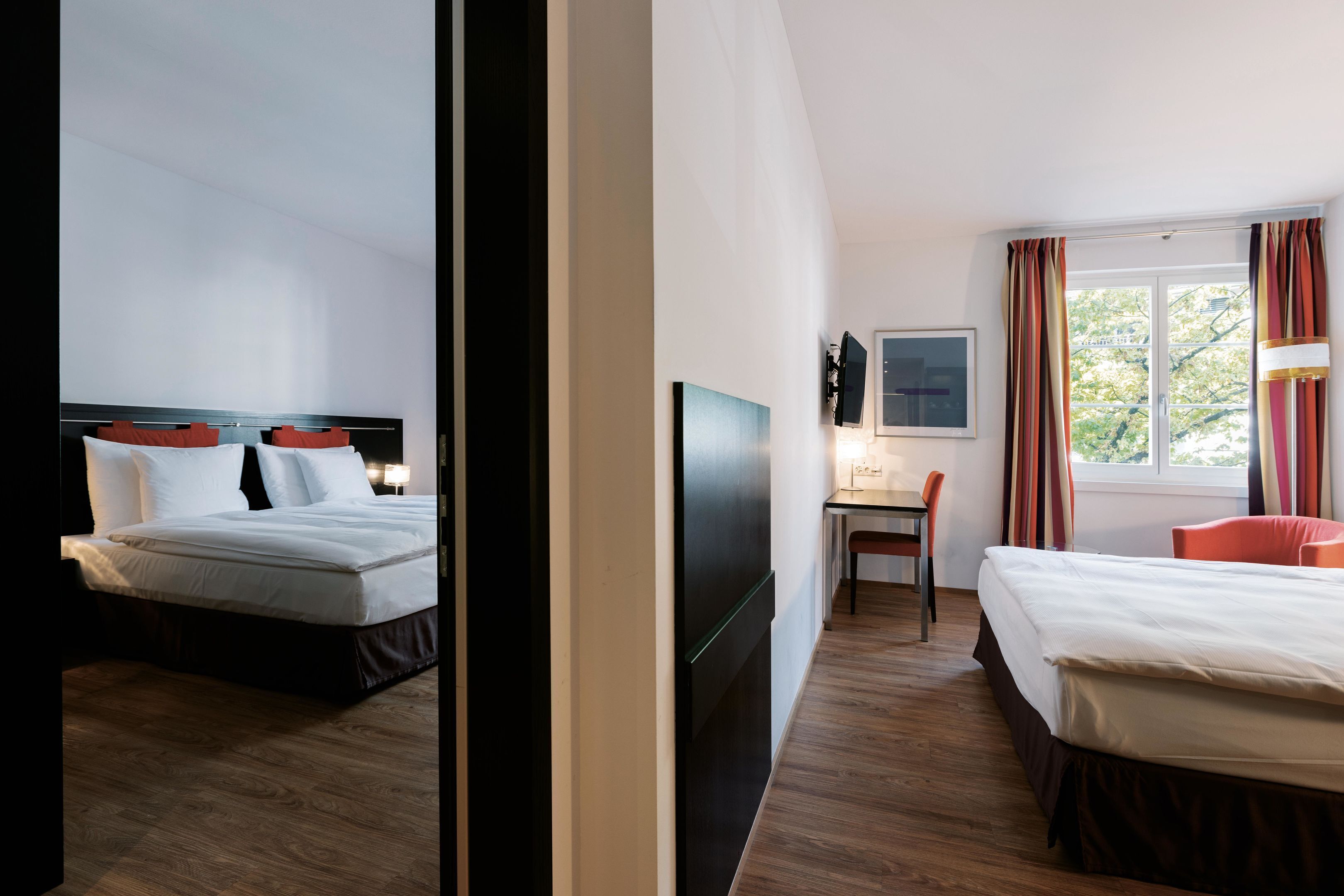 A hotel room with two beds, a desk, a chair, a TV, and a window with curtains.