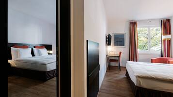A hotel room with two beds, a desk, a chair, a TV, and a window with curtains.