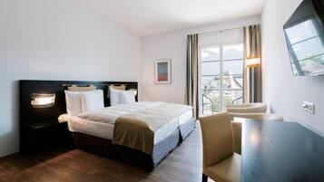 A hotel room with a bed, bedside table, chair, and a large window with a view.