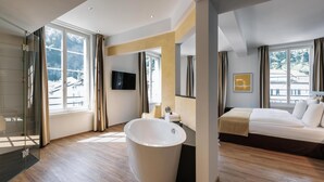A modern hotel room with a large bathtub, a bed, and a TV.