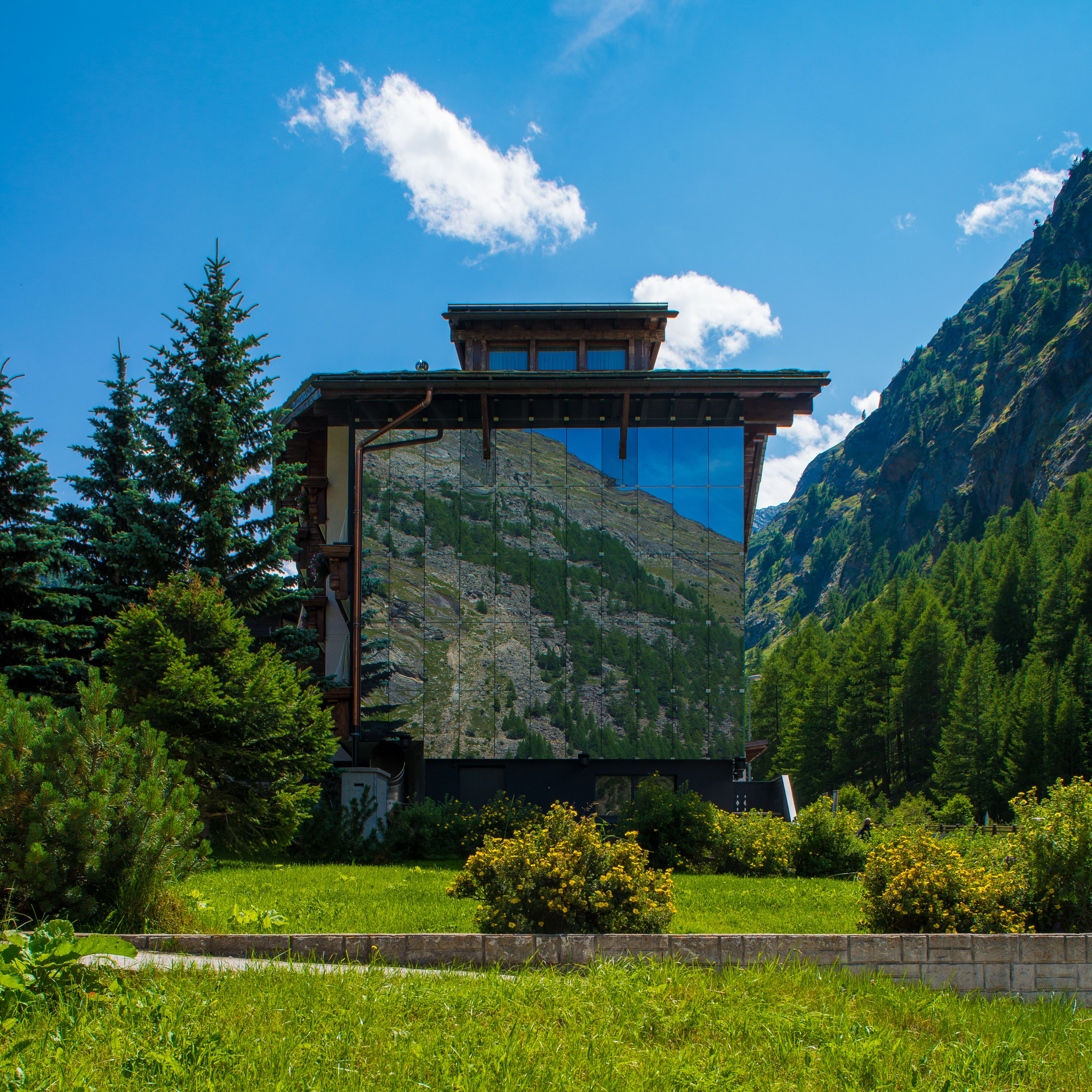 A mountain lodge with a large glass facade, surrounded by lush greenery and mountains.