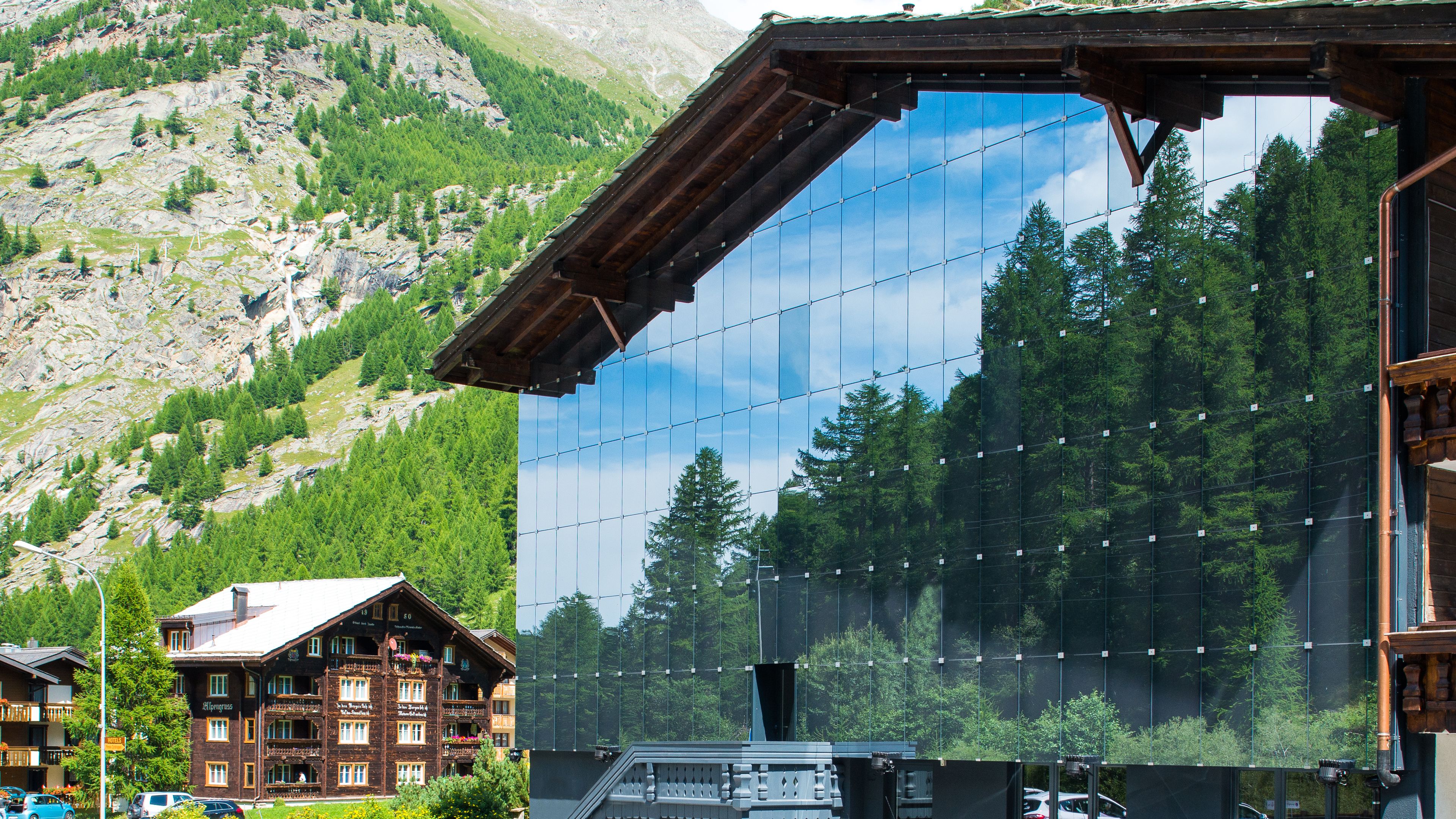 Un chalet de montagne à la façade en bois, doté de grandes fenêtres et offrant une vue sur la forêt et les montagnes environnantes.