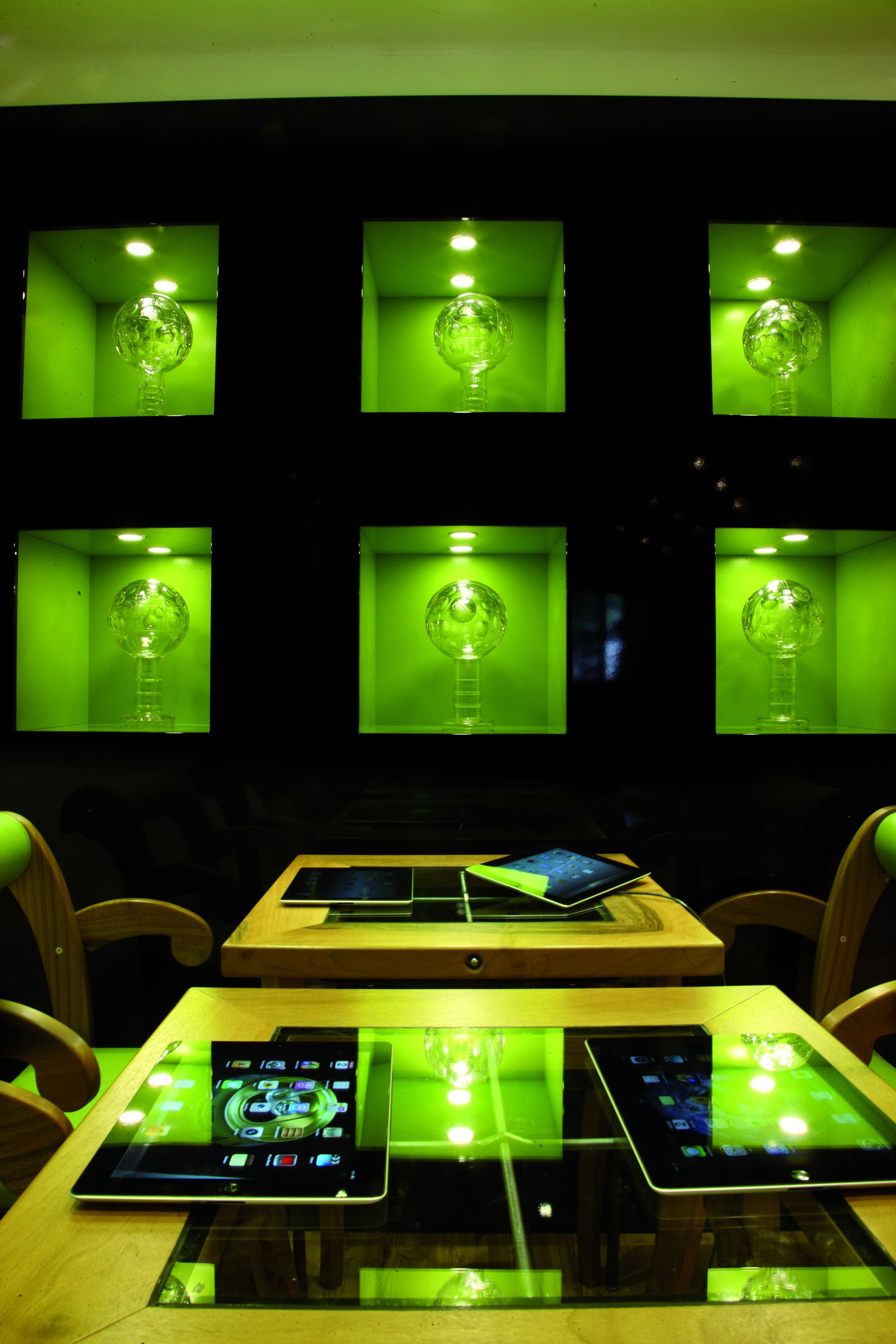 A room with a glass table displaying multiple tablets and a wooden table with a laptop.