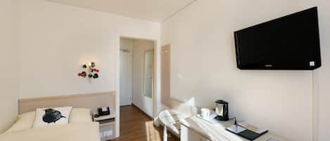 A hotel room with a bed, a desk with a flat-screen TV, a chair, and a small table.