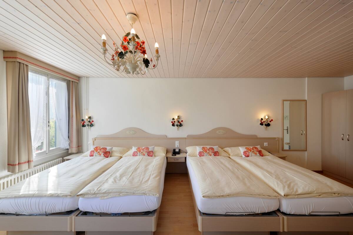 A hotel room with two beds, a chandelier, a mirror, and a window with curtains.