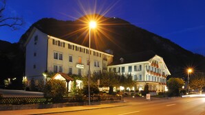 Ein Hotel mit mehreren Stockwerken, Bergkulisse und beleuchteten Straßenlaternen.