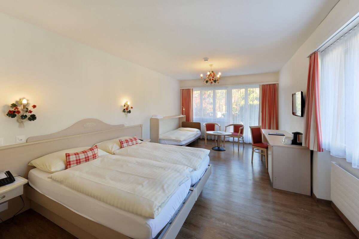 A hotel room with a large bed, a desk, a chair, and a small table.