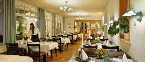 Een restaurant met meerdere gedekte tafels, een ober die gasten bedient en een warme, uitnodigende sfeer met houten vloeren en decoratieve verlichting.
