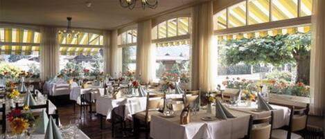 Comedor con mesas dispuestas para el servicio, ventanas amplias con cortinas y un candelabro.