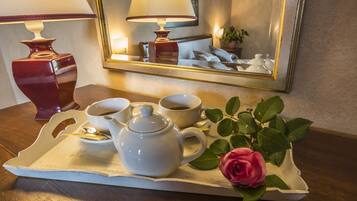 A tray with a teapot, cups, and saucers, a rose, and a mirror reflecting a lamp and a bed.
