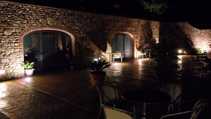 An outdoor patio area with stone walls and arched doorways, featuring tables and chairs.
