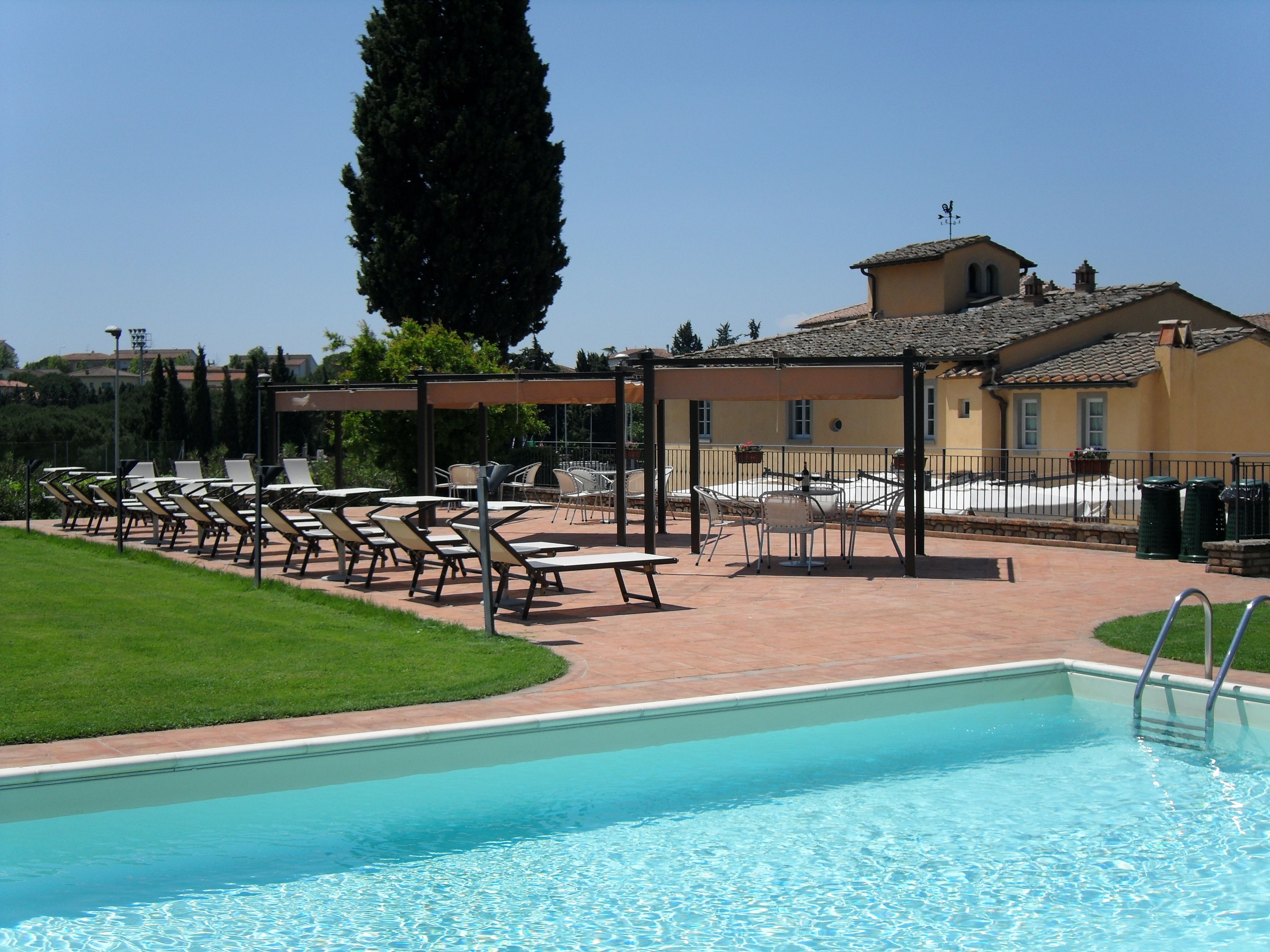 Uma área de piscina com espreguiçadeiras, um pérgola e um edifício com telhado em azulejos.