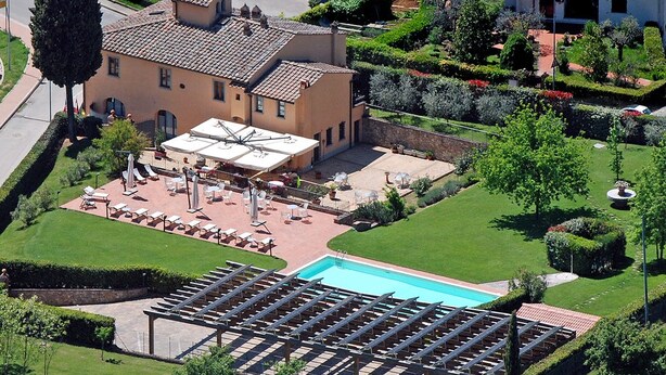 An aerial view of a hotel with a swimming pool, outdoor seating area, and well-maintained gardens.