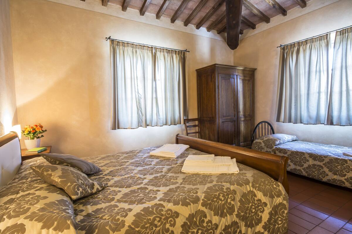 Un dormitorio con dos camas, un armario de madera y una mesita de noche con un jarrón de flores.