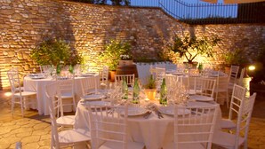 An outdoor dining area with stone walls and white tables and chairs.