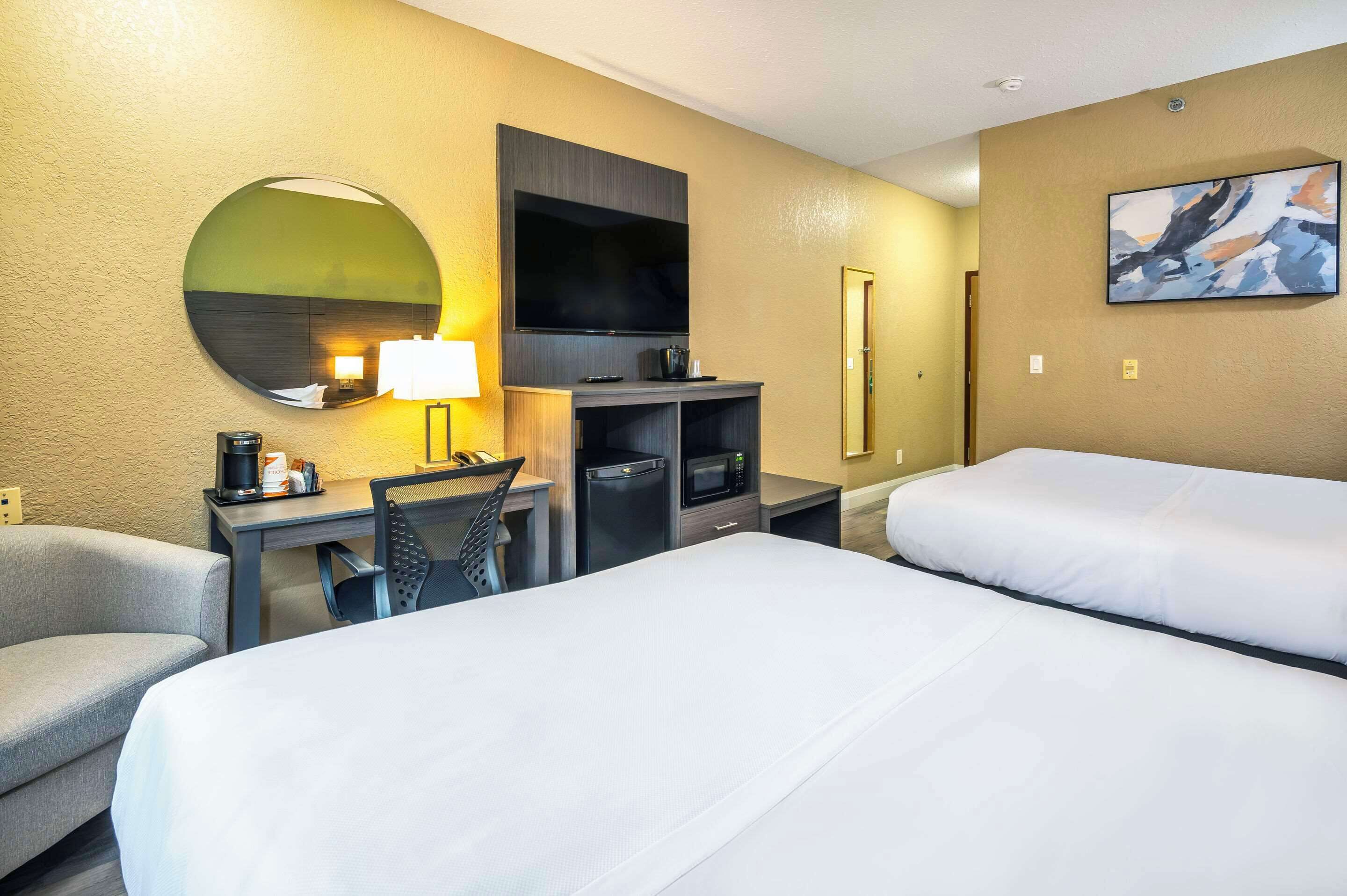 A hotel room with two beds, a desk with a chair, a TV, a coffee maker, and a microwave.