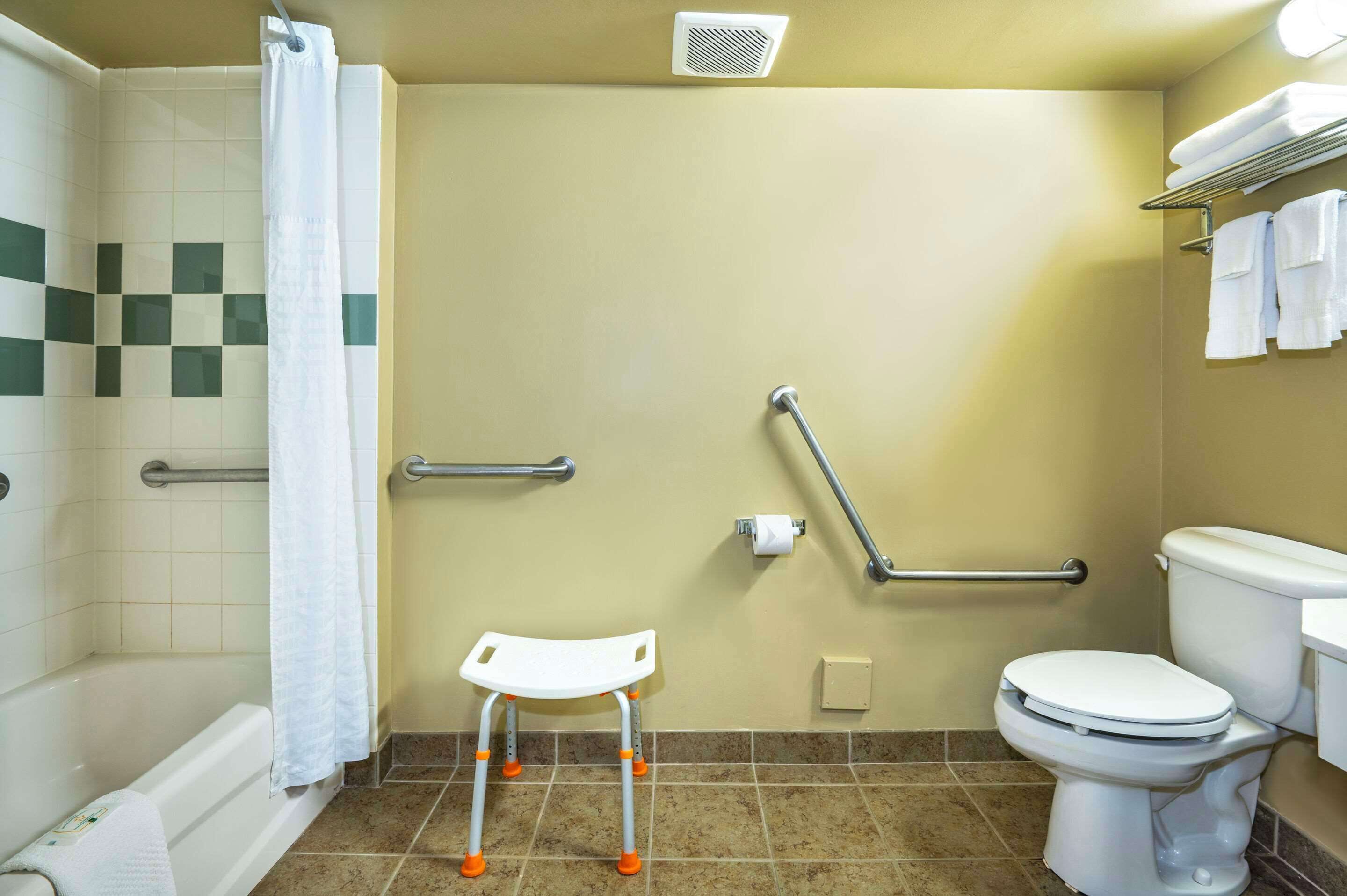 A bathroom with a shower, toilet, grab bars, and a wheelchair-accessible bench.