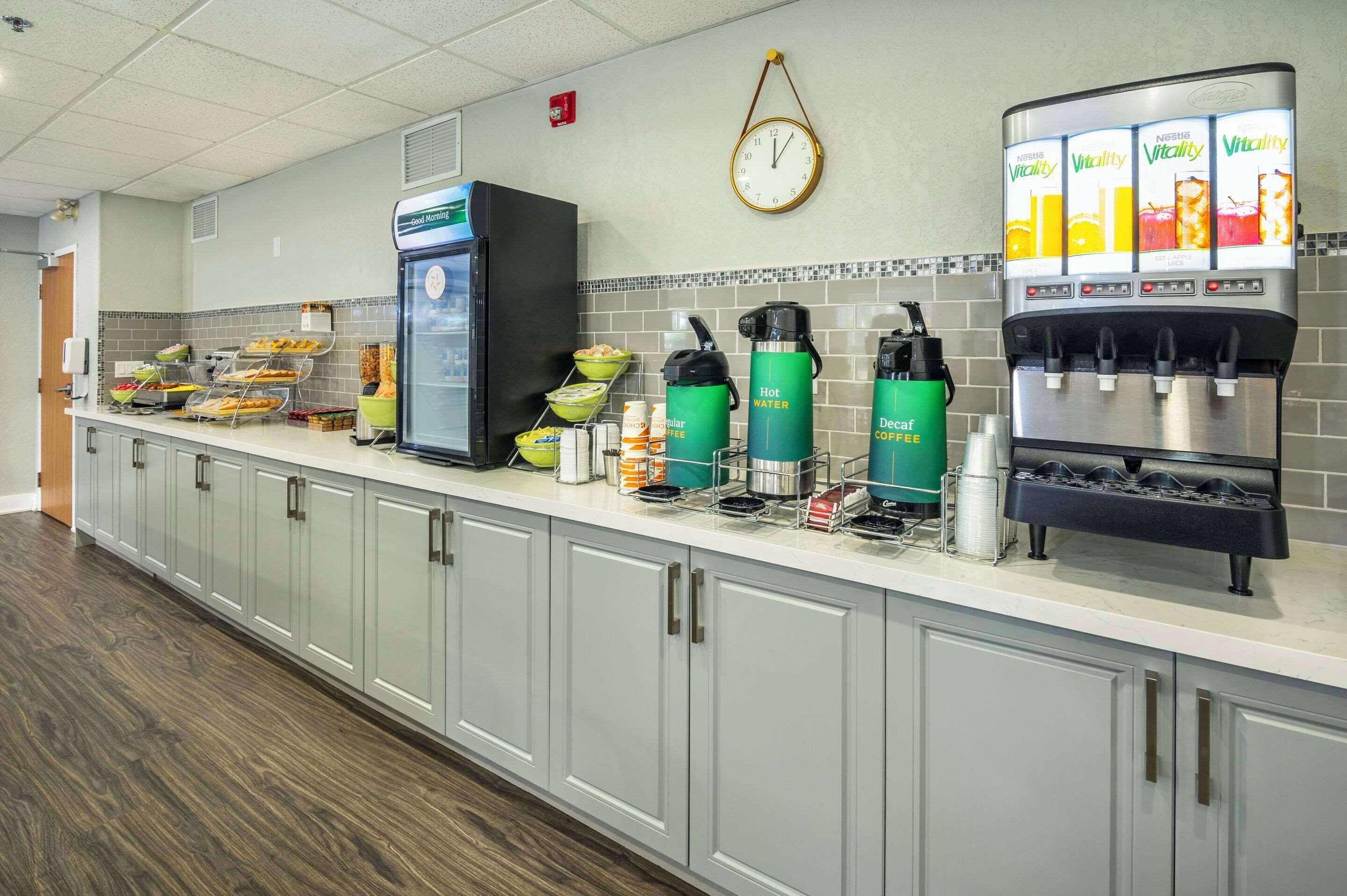 Una cucina d'hotel con un angolo caffè, una sveglia e un distributore di succo di frutta.