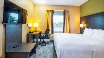 Quarto de hotel com cama, escrivaninha, cadeira, televisão e duas luminárias.