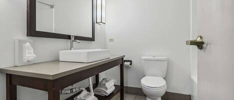 A modern bathroom with a white sink, mirror, and toilet. There is a towel rack with folded towels and a shelf with shoes.