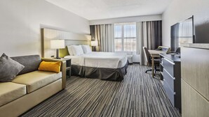 A hotel room with a bed, a desk, a chair, a sofa, and a TV.
