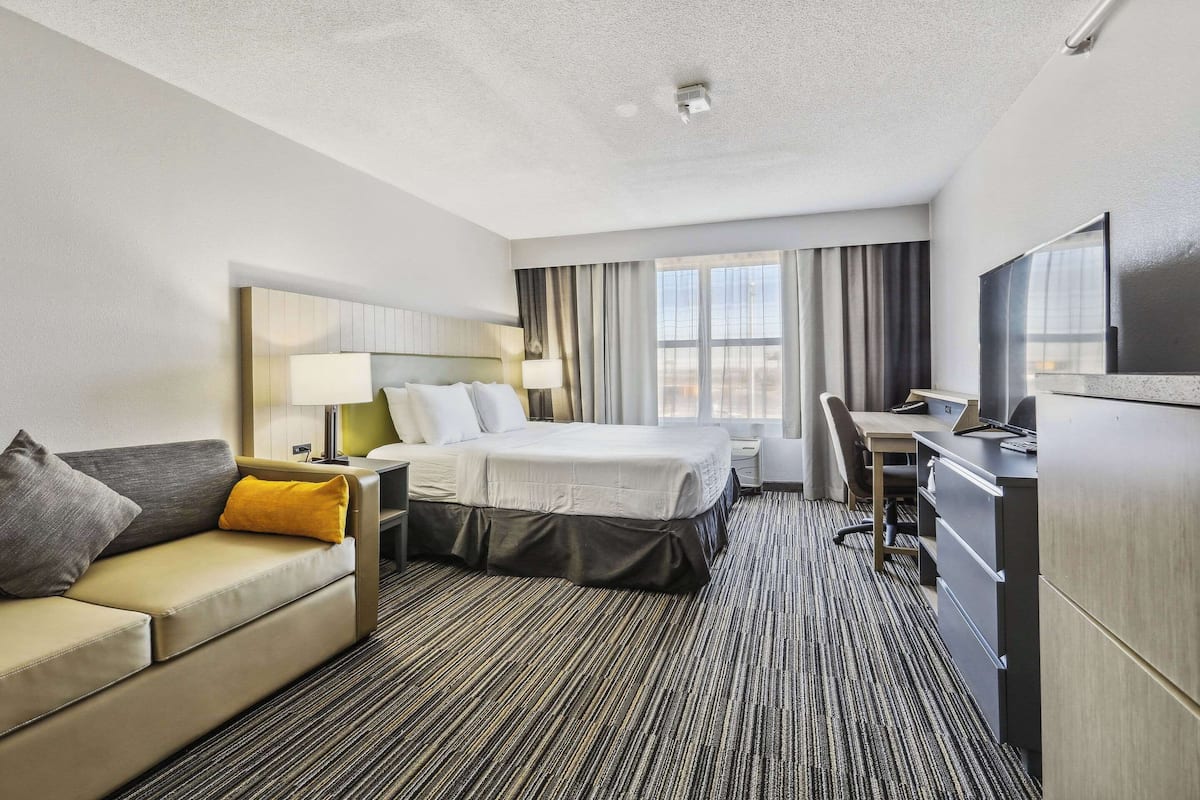 A hotel room with a bed, a desk, a chair, a sofa, and a TV.