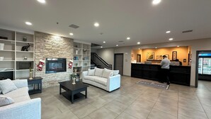 A modern hotel lobby with a reception desk, a staircase, and a seating area with a sofa and coffee table.
