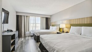 A hotel room with two beds, a desk, a TV, and a window with curtains.