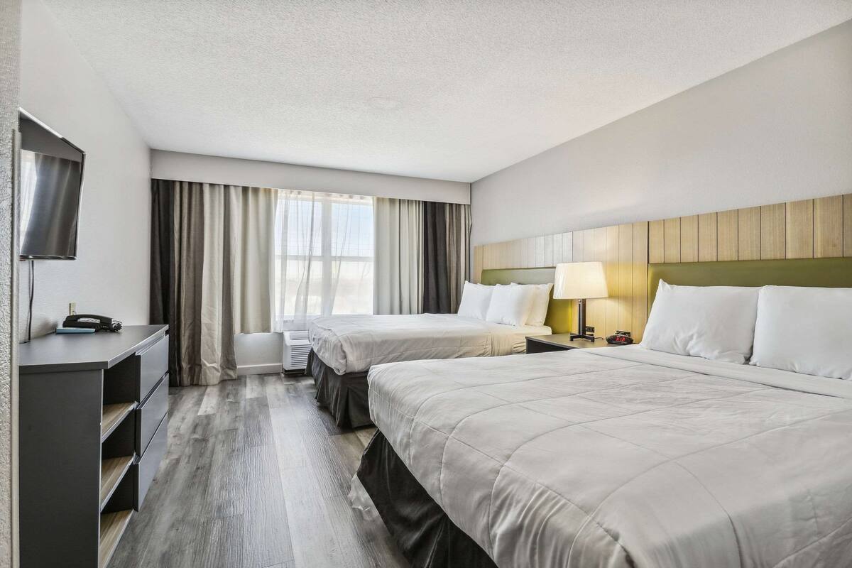 A hotel room with two beds, a desk, a TV, and a window with curtains.