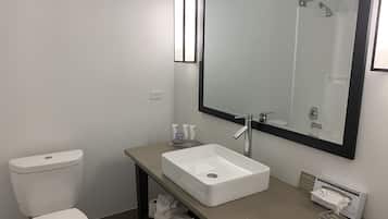 A modern bathroom with a white toilet, a beige sink, and a large mirror.